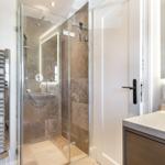 Shower cabin with glass enclosure, bathtub, and sink with mirror.