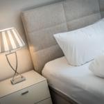 Bed headboard with white pillows and bedside table with lamp.