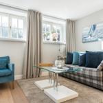Living room with sofa, armchair, glass table, and wall art of sailboats.