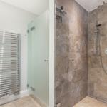 Shower with stone wall and handheld shower. Heater on the wall.