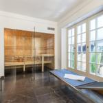 Sauna with wooden bench and glass wall. Outdoor area with windows and loungers.