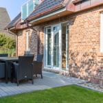 Terrasse mit Tisch und Stühlen neben einem Haus mit Backsteinfassade.