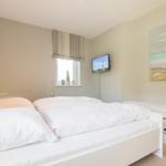 Schlafzimmer mit weißem Bett, Fenster, Wandbild und Fernseher.