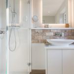 Bad mit Dusche, Waschbecken und beleuchtetem Spiegel.