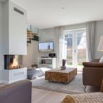 Wohnzimmer mit Kamin, Sofa und TV. Durchgang zur Küche. Terrasse mit Blick aufs Haus.