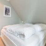 Schlafzimmer mit Doppelbett, Nachttisch und Bild an der Wand. Tür führt in die Badezimmer.