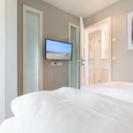 Schlafzimmer mit Bett, Fernseher und Blick in Bad