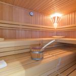 Sauna mit Holzbänken, Thermometer und Eimer mit Löffel.