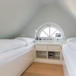 Two beds under a skylight with nightstand and lamps.