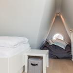 Room with sloped ceilings, white bed, and round window