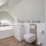 Bath with sink, toilet, and shower tub under sloped ceiling.