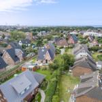 Aerial view of residential area with houses, gardens, and distant sea.