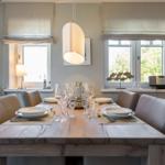 Dining room with wooden table, chairs, and windows with roller blinds.