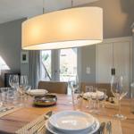 Dining room with wooden table, chairs, and pendant light. Windows and skylight provide daylight.