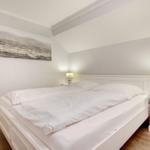 Schlafzimmer mit weißem Bett, Nachttischen und Wandbild.