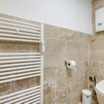 Badezimmer mit Heizkörper, Toilette und Toilettenpapierhalter an Steinwand.