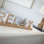 Auf dem Schreibtisch steht ein Holzschild mit der Aufschrift RELAX und eine Lampe.