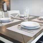 Esszimmertisch mit Platz für vier Personen, weißer Tisch, Holzoptik, Teller, Gläser und Besteck.