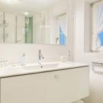 Badezimmer mit Waschbecken, Spiegel und Fenster mit Vorhang.