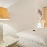 Schlafzimmer mit weißem Bett, Nachttisch und Lampe. Hinter dem Bett steht ein Schrank.