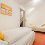 Zwei Betten mit weißen Laken und gelben Kissen. Orange Teppich und Wandbild mit Strandmotiv.