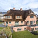 Haus mit strohgedecktem Dach und Backsteinfassade mit Terrasse und Garten.