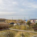 Blick auf Parkplatz, Dünen und Meer mit moderner Geländerbrüstung.
