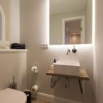 Badezimmer mit Waschbecken, Spiegel und Toilette. Fenster mit Jalousie.