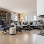 Wohnzimmer mit Sofa, Sessel und Kamin. Holzboden und Fenster.
