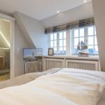 Schlafzimmer mit Dachschrägen, Fenster, TV und Blick in die Badewanne.