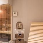 Sauna mit Glaswand, Holzbänken und kleinem Schrank mit Körben.