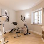 Fitnessraum mit Fahrradtrainer und Laufband, Wandbild und Fenster.