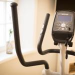 Elliptisches Fitnessgerät mit Display und Griffen in einem Raum mit Fenster.