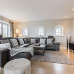 Wohnzimmer mit grauem Sofa, Holzboden und drei Bogenfenstern.