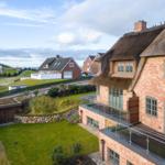 Haus mit Strohdach und Terrasse, Grünfläche und Blick aufs Meer.