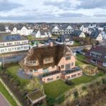 Dorfhaus mit Strohdach und Garten. Blick auf Wohngebiet mit Häusern und Straßen.
