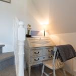 Desk with chair under sloped ceiling, next to staircase with white balustrade.
