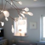 Modern ceiling light with many white lamps above a living area with windows.