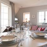 Set dining table with plates and glasses. Sofa with cushions in background.