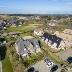 Aerial view of houses with gardens and parking areas in a rural setting.