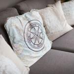 A gray sofa with cushions, one with compass pattern, others with text and ornaments.