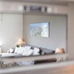 Living room with sofa, cushions, and wall art. View through a mirror frame.