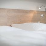 Wooden headboard with wall lamp and white bedding.