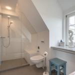Bathroom with shower, toilet, and window with sea horse decorations.