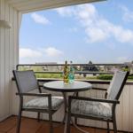 Balcony with table and two chairs. View of rooftops and sky.