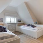 Room with two beds, sloped ceilings, and window with roller blind.