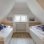 Two single beds under sloped ceilings with window and wooden floor