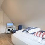 Bedroom with bed, TV, and chair under sloped ceiling.