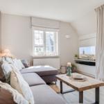 Living room with sofa, wooden table, and TV. Windows and door provide light.