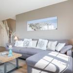 Living room with gray sofa, wooden table, and wall art. Staircase in background.